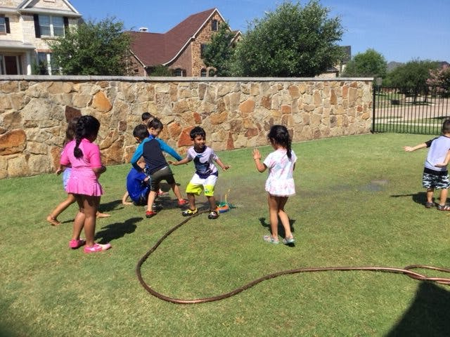 Children playing with a sprinkler in a grassy yard