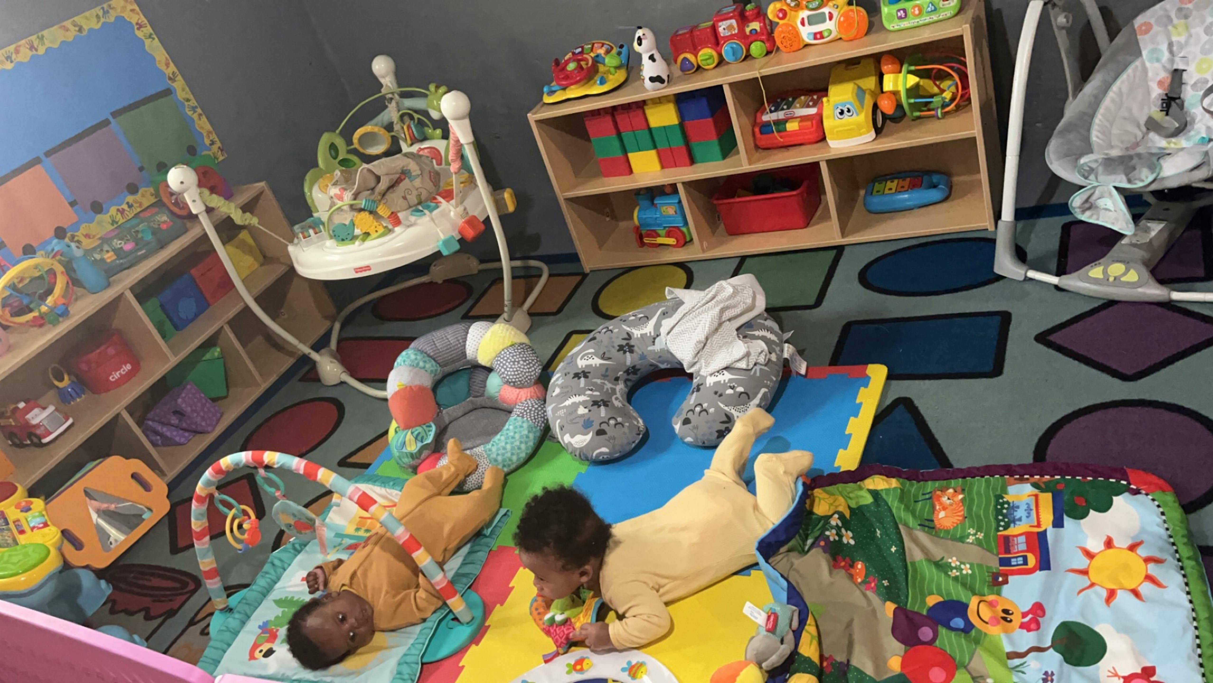 Two children playing on mats in a room with toys and shelves
