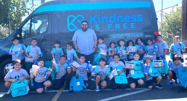 Adult and children standing and kneeling in front of a van with text "Kindness Is Free"