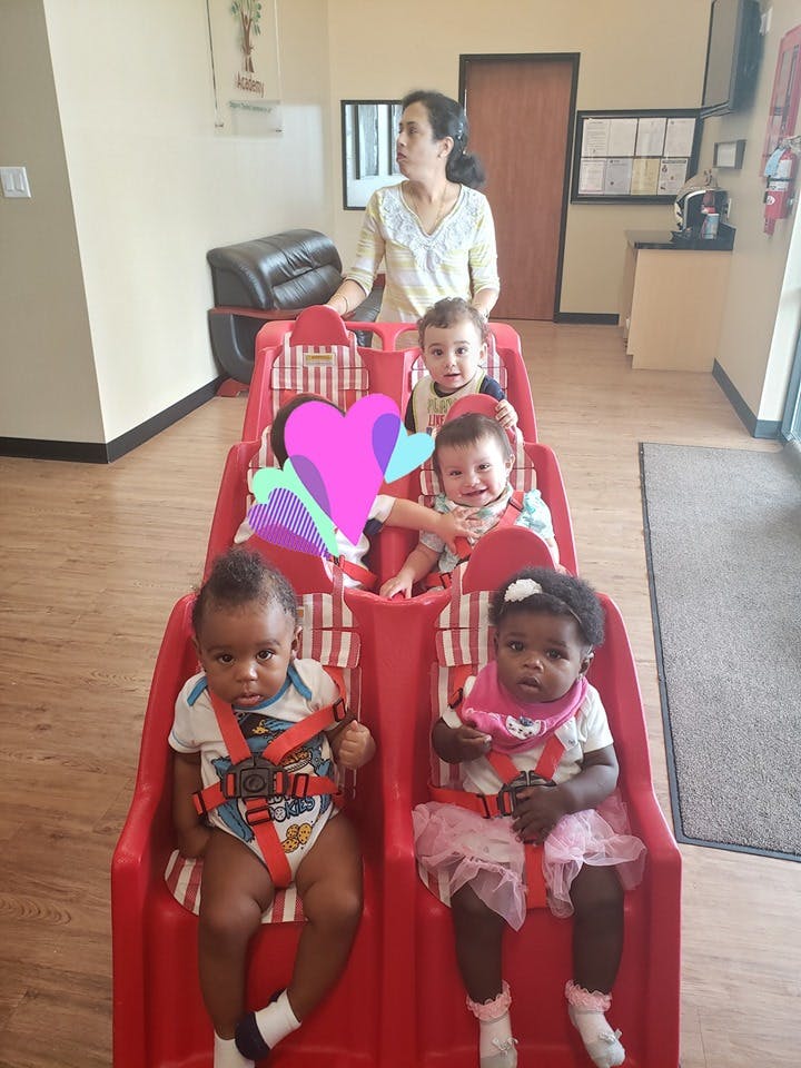 Person standing behind multiple children seated in a red multi-seat stroller