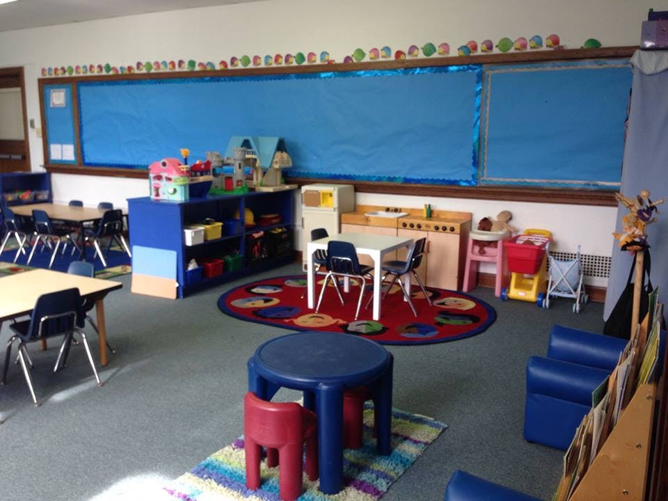 Classroom with small tables and chairs, blue bulletin board, and play area