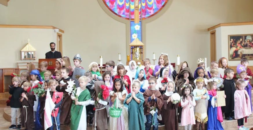 Group of children in costumes standing in a room with a person at a podium