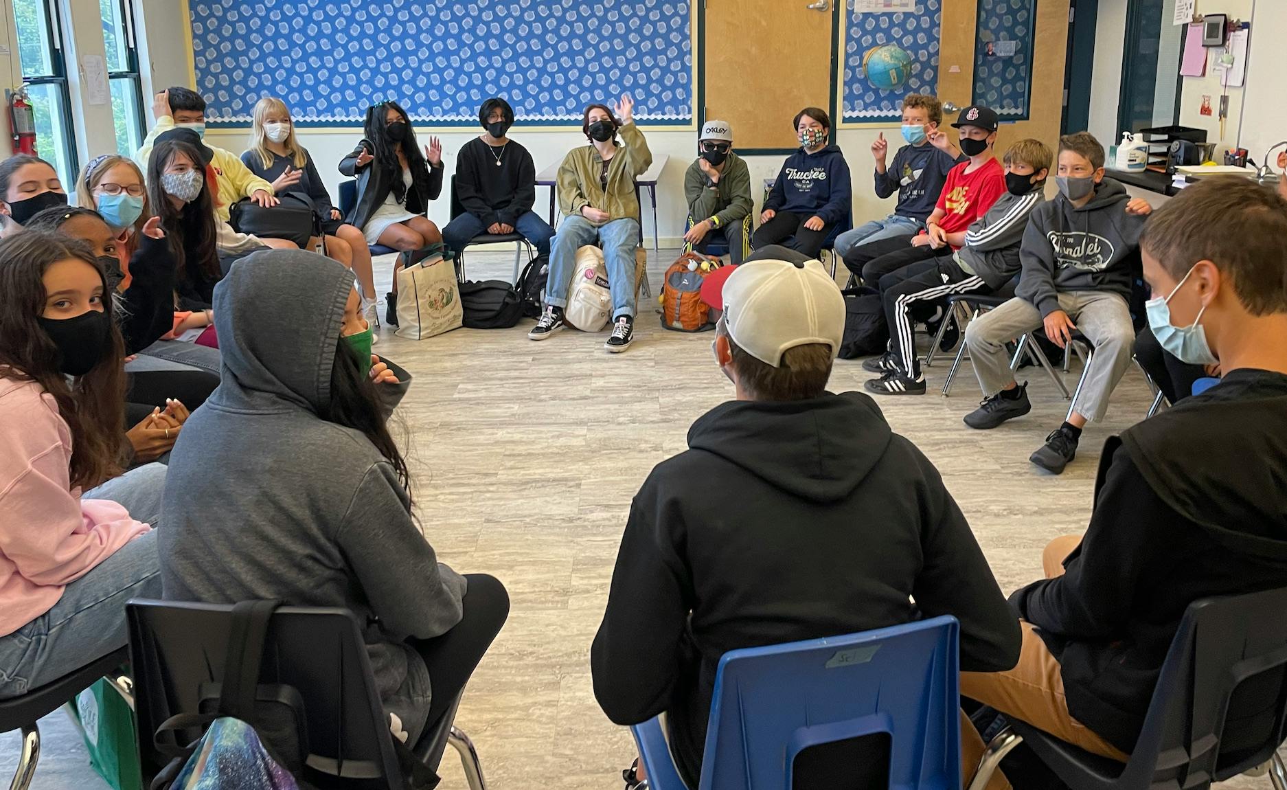 Group of teens and children sitting in a circle, some raising their hands