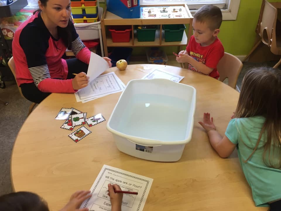 Adult and children at a table with papers and a white bin