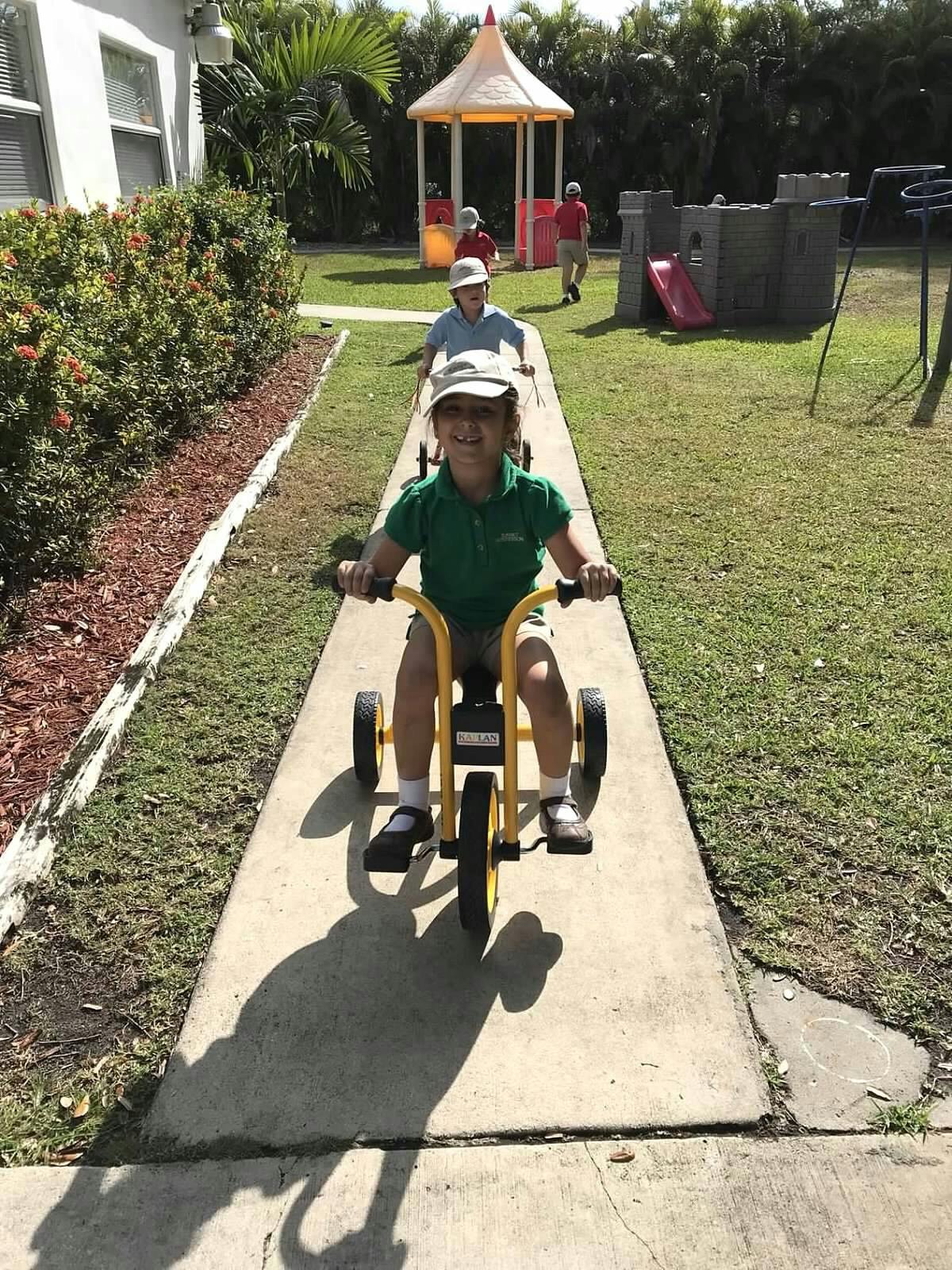 Child riding a tricycle on a sidewalk with other children in the background