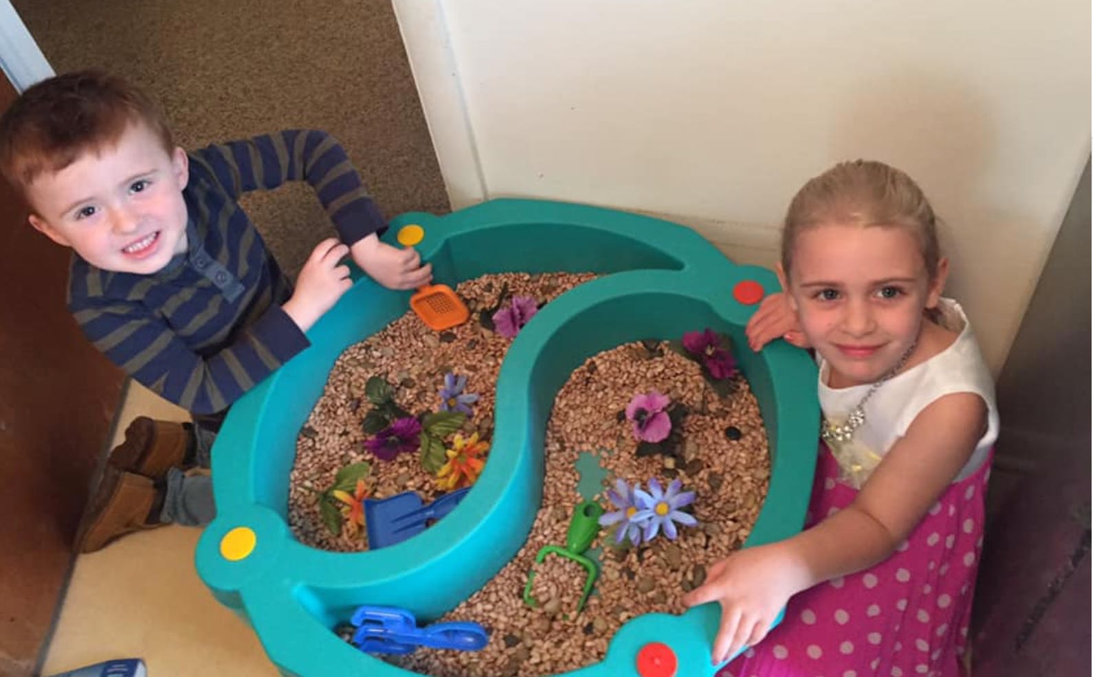 Two children playing with a sensory table filled with sand and toys