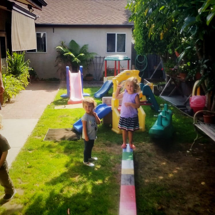 Two children playing in a backyard with slides and a balance beam