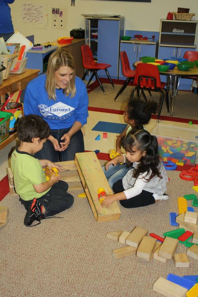 Adult and children playing with blocks on the floor in a classroom