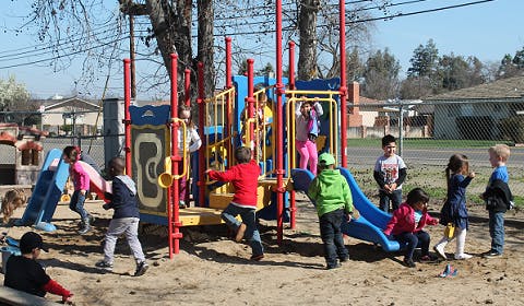 Children playing on a playground structure with slides and climbing structures