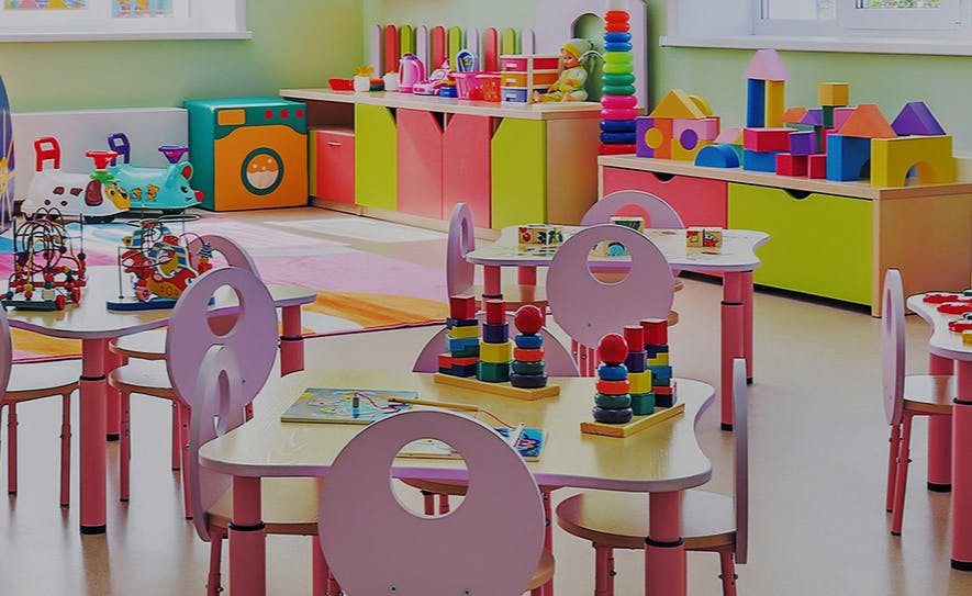 Empty classroom with small tables and chairs, toys on shelves and tables