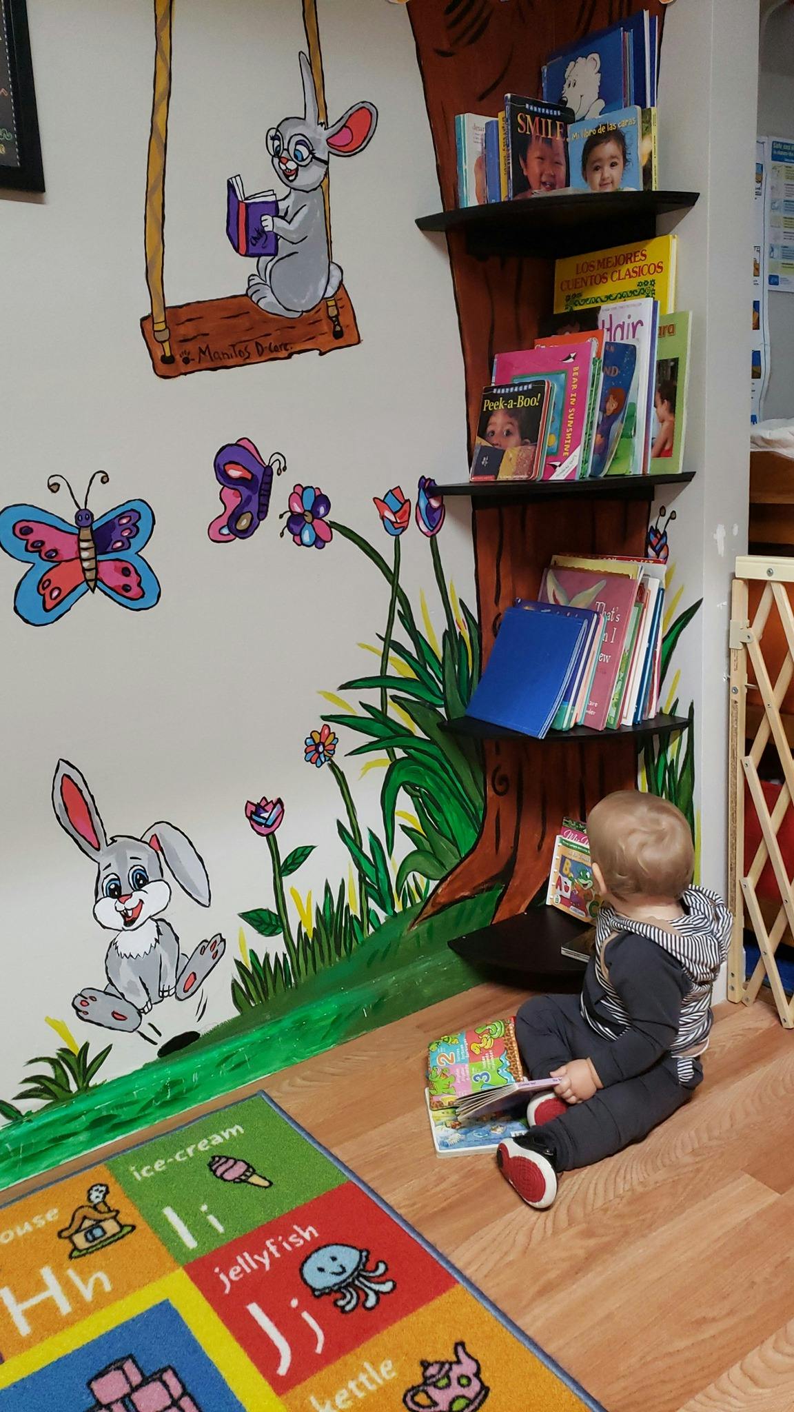 Child sitting on floor reading a book next to a wall mural