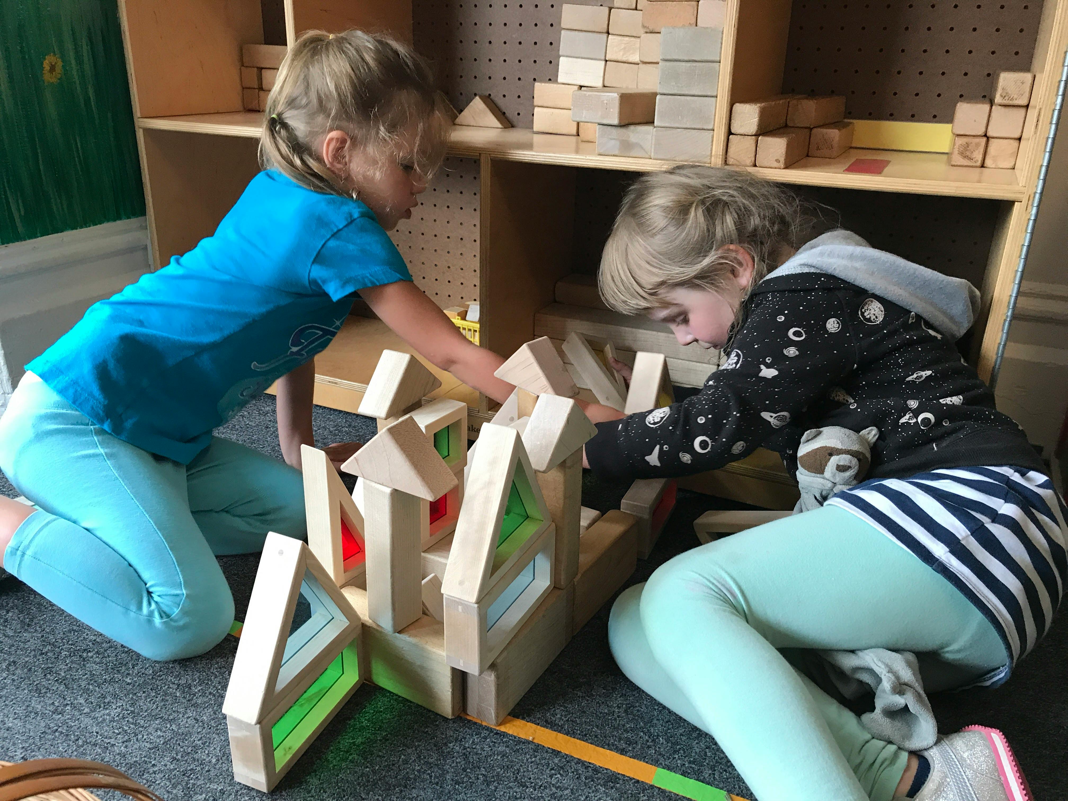 Two children playing with wooden blocks on the floor