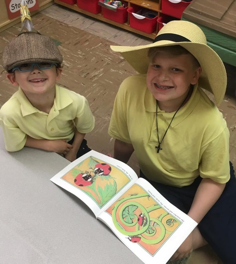Two children wearing hats looking at an open book with illustrations