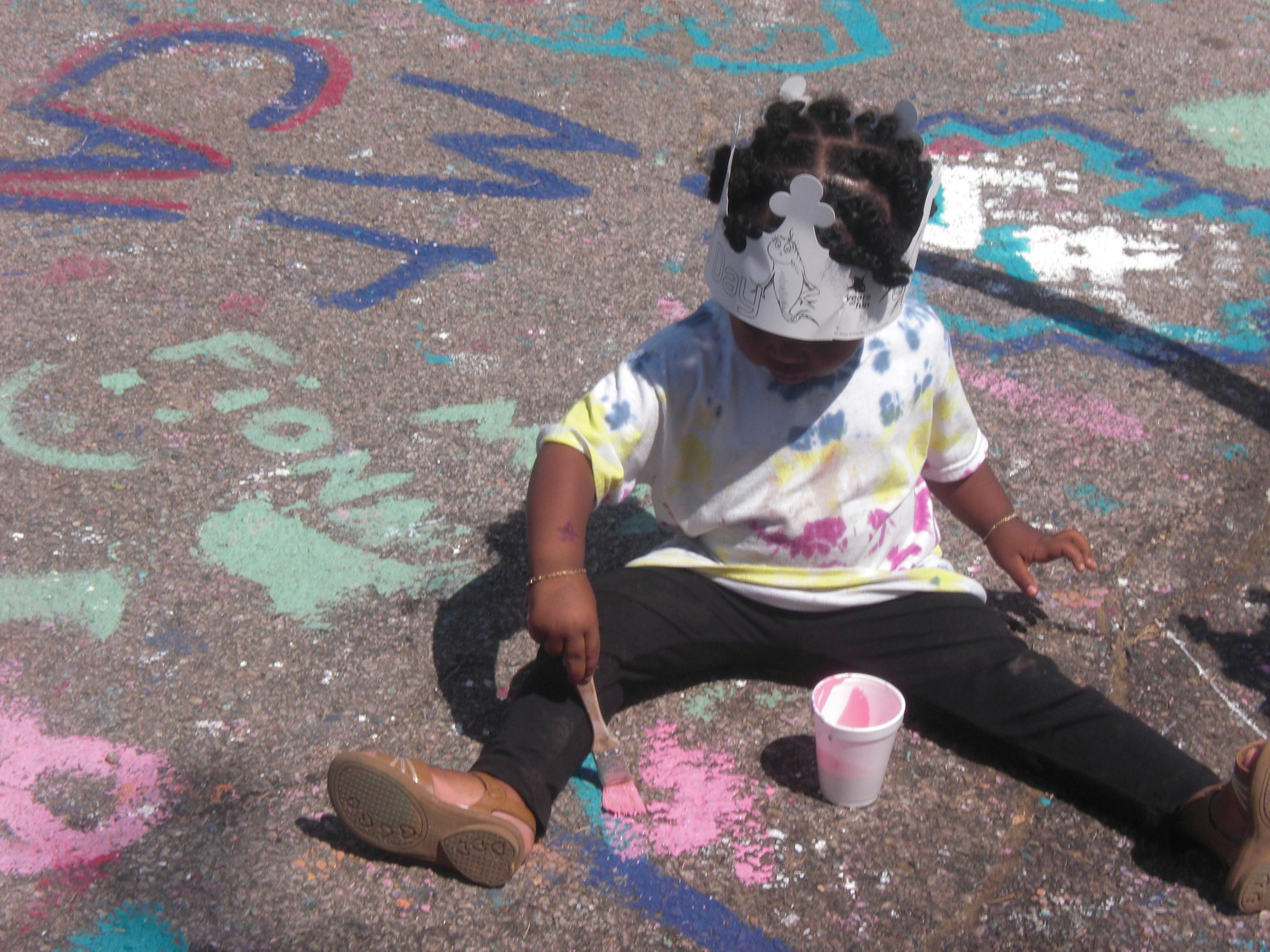 Child sitting on ground painting with brush and cup