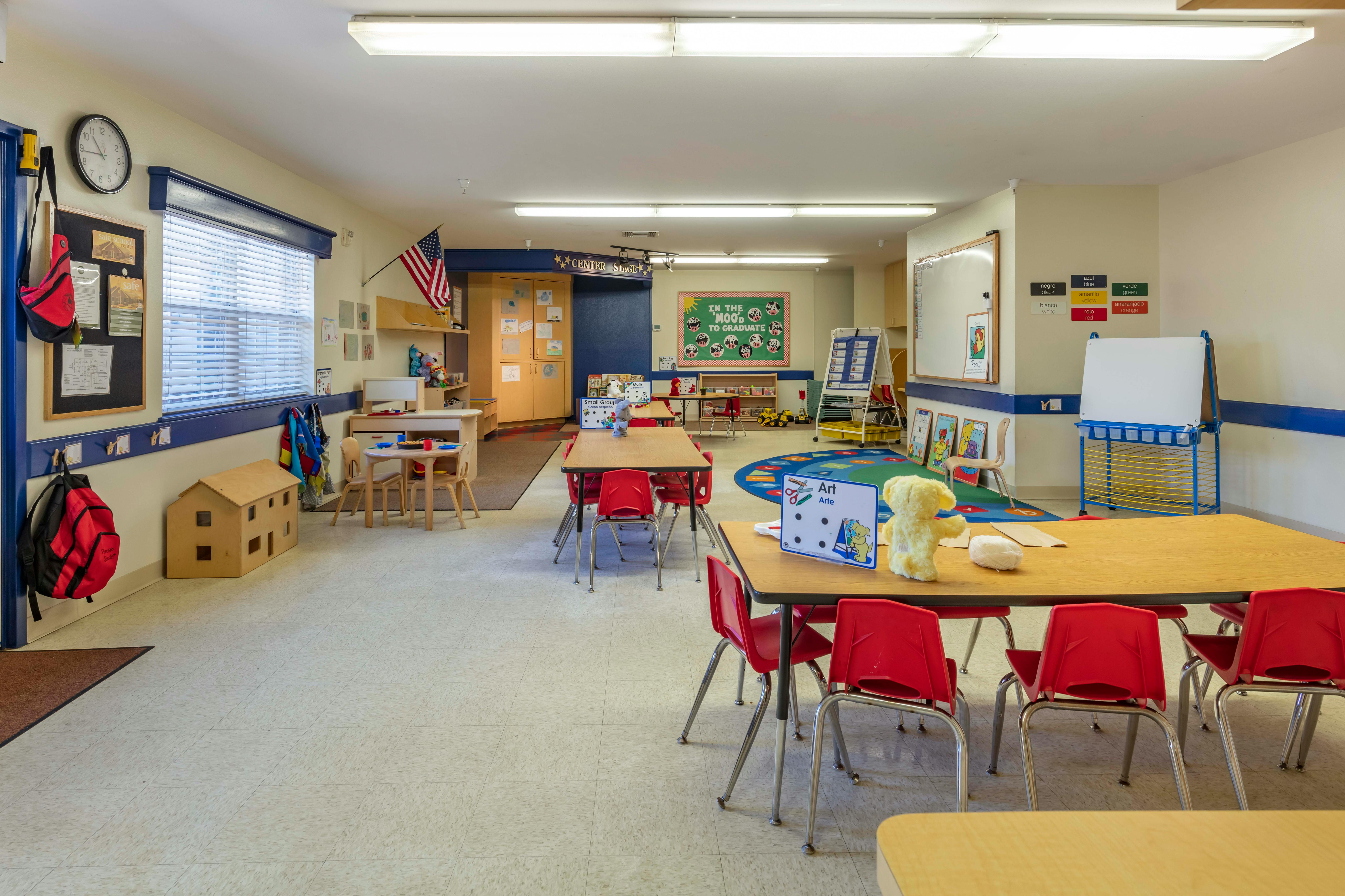 A colorful empty classroom with small tables and chairs, and learning materials