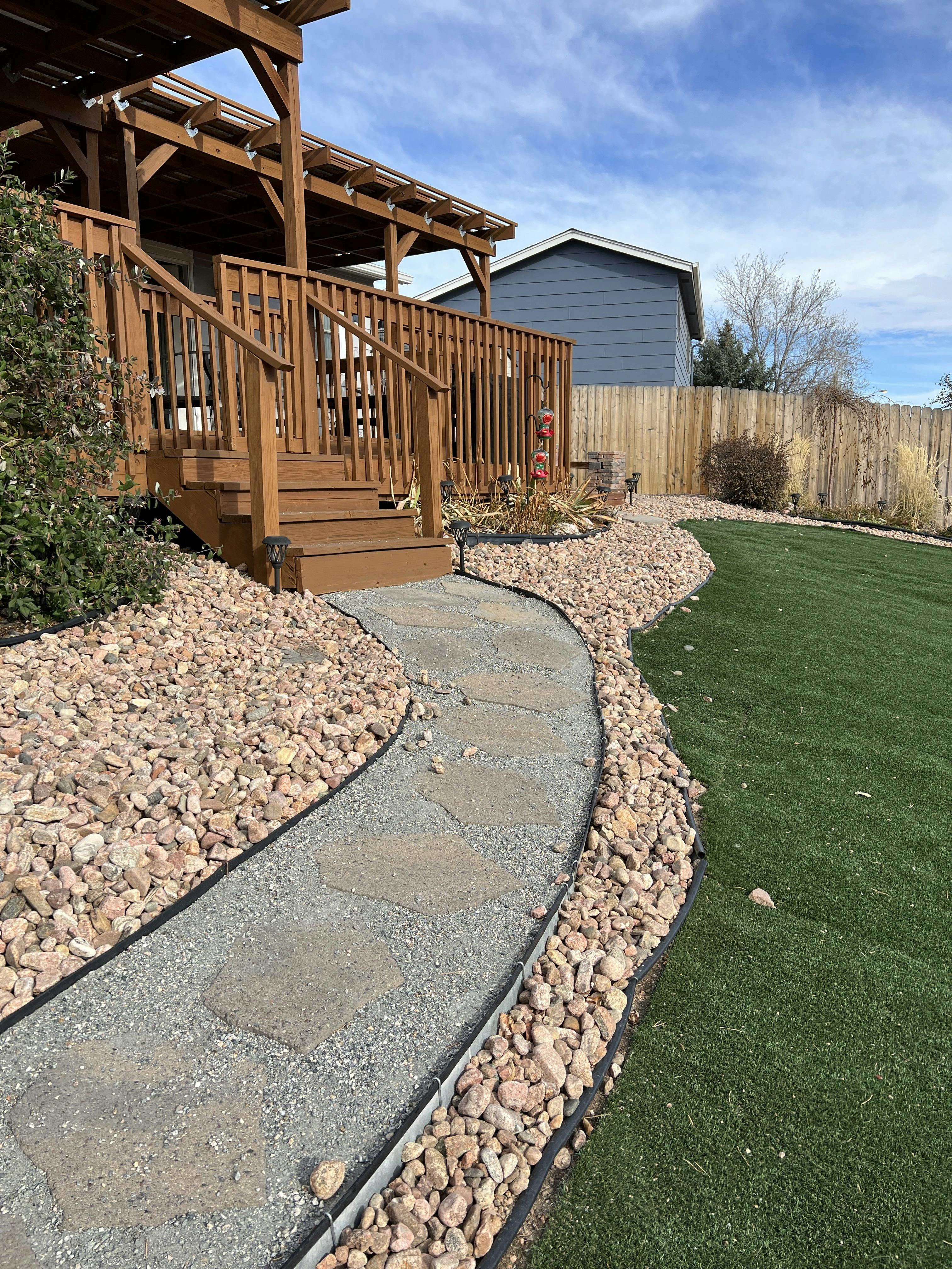 Wooden deck with stairs next to a stone path and green lawn