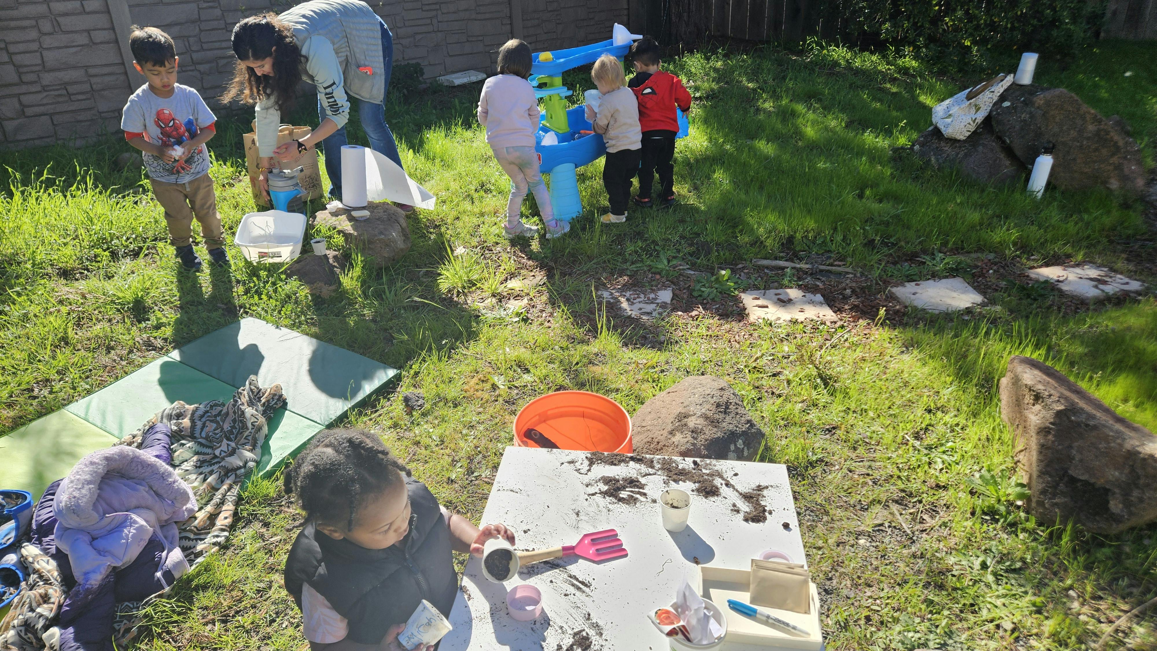 Adult and children playing outdoors with water and mud