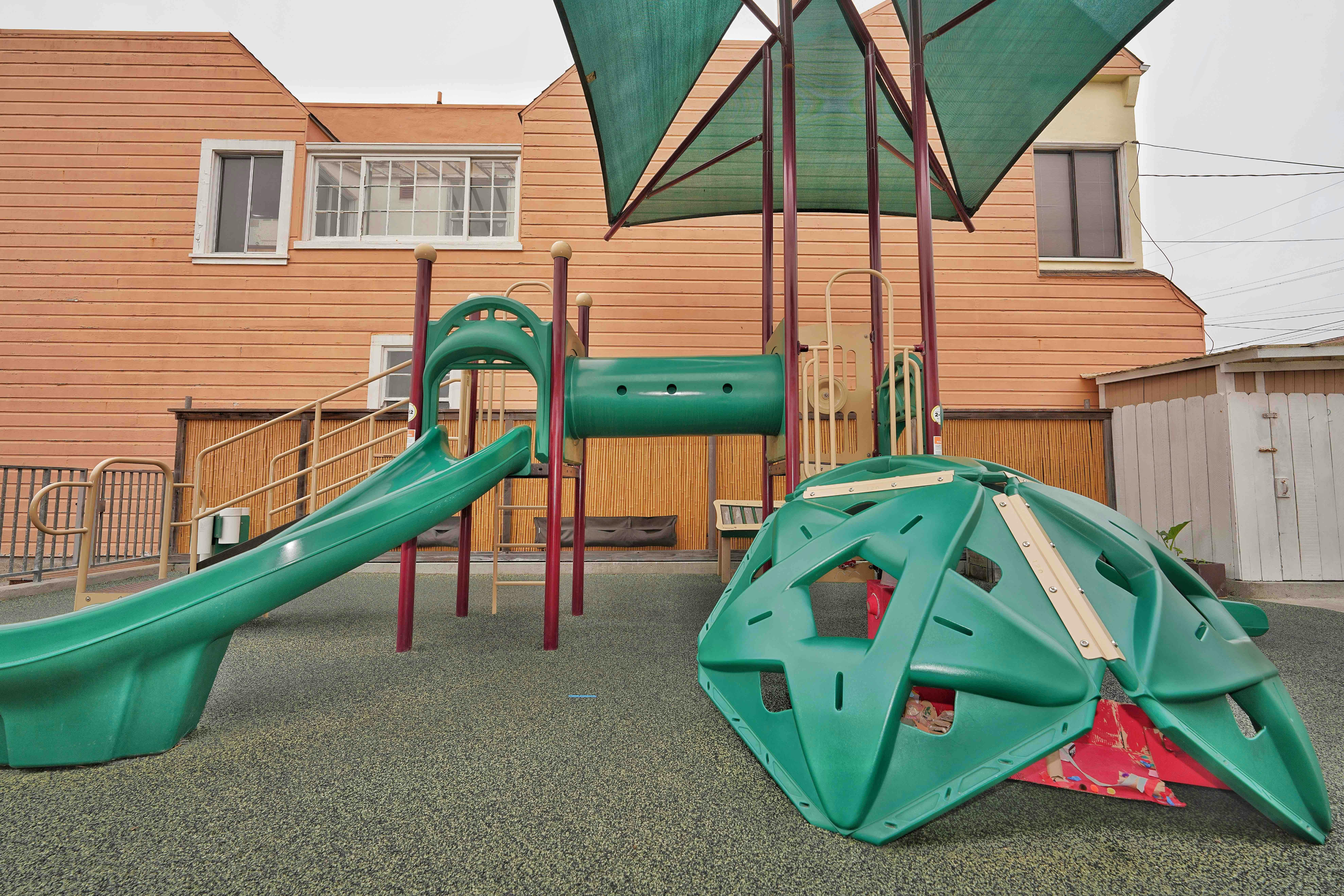 Playground equipment with a slide and climbing dome under a shade canopy