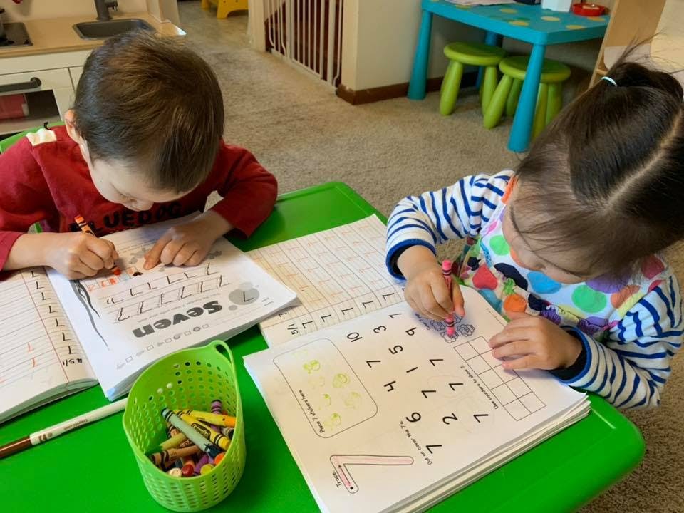Two children writing in workbooks at a table
