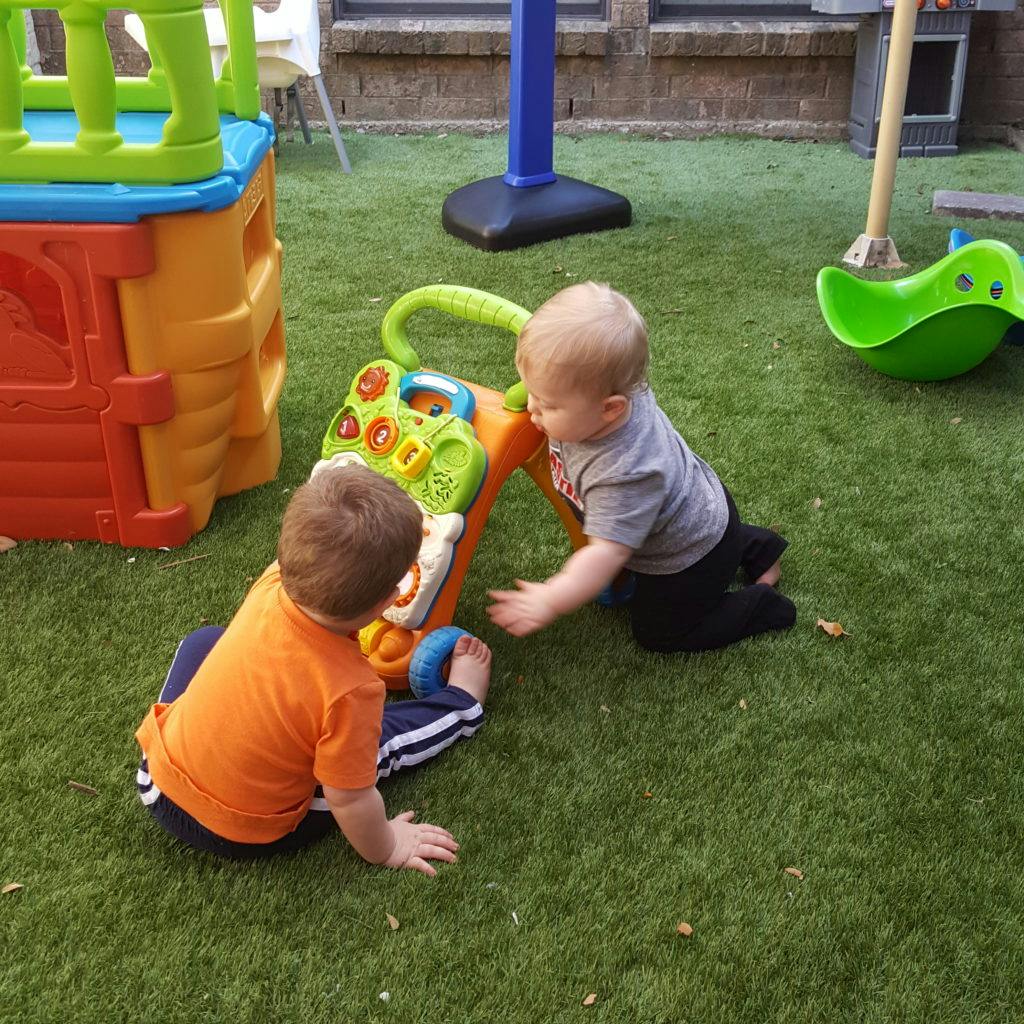 Two children playing with a toy on artificial grass