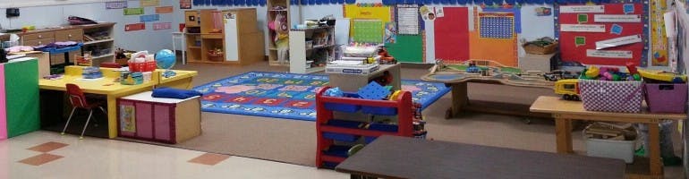 A classroom with colorful tables, chairs, and a rug