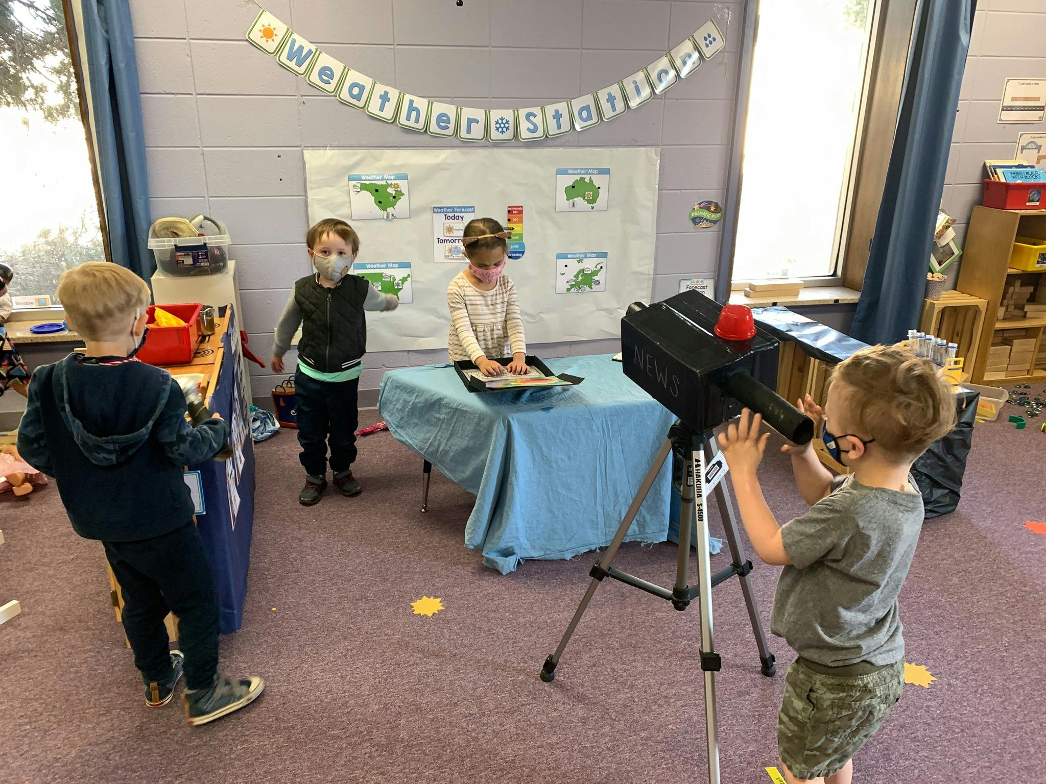 Children playing with a camera and weather board in a classroom
