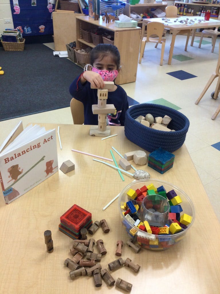 Child in a pink mask playing with wooden blocks at a table
