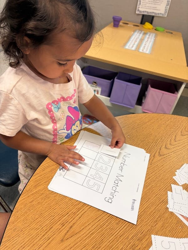Child matching numbers on a worksheet with "Number Matching" visible