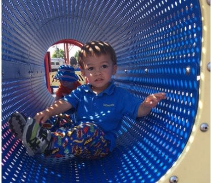 Child sitting inside a blue playground tunnel