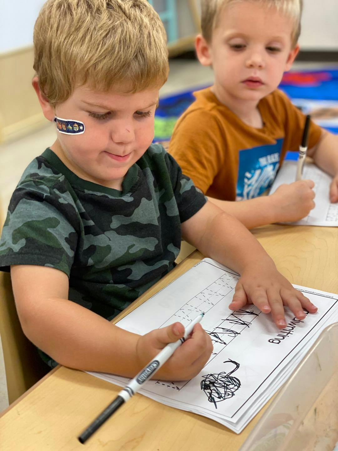 Two children writing at a table in a classroom