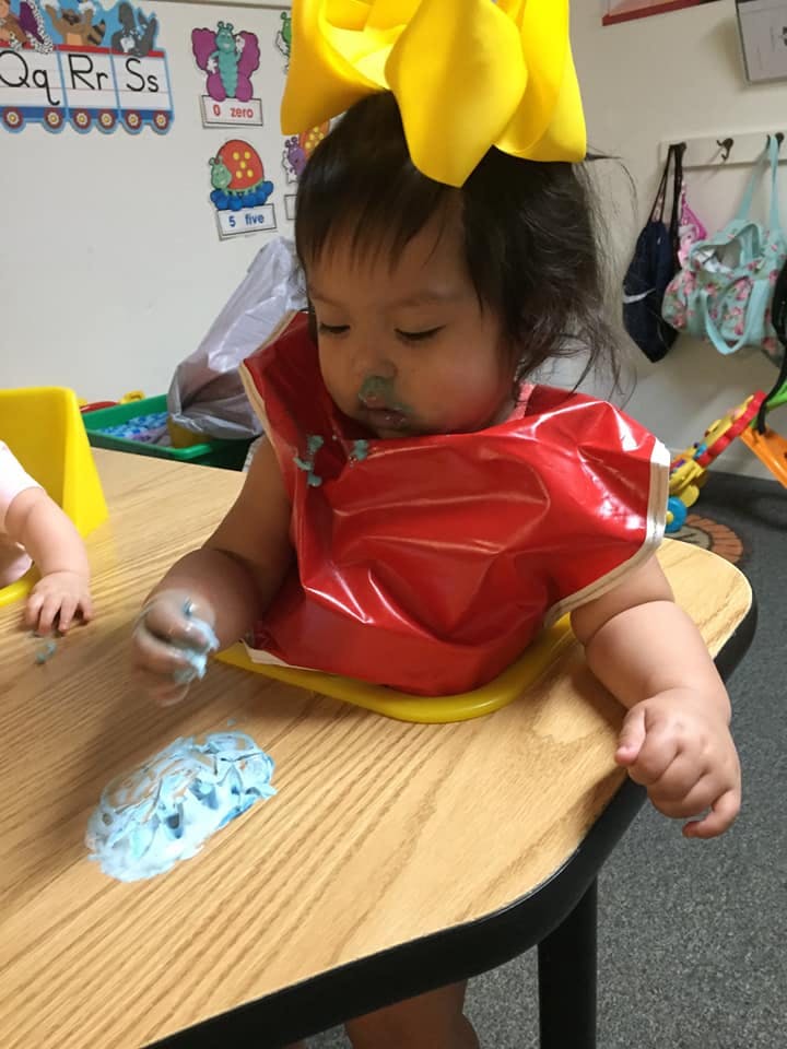 Child in a red bib playing with blue playdough at a table