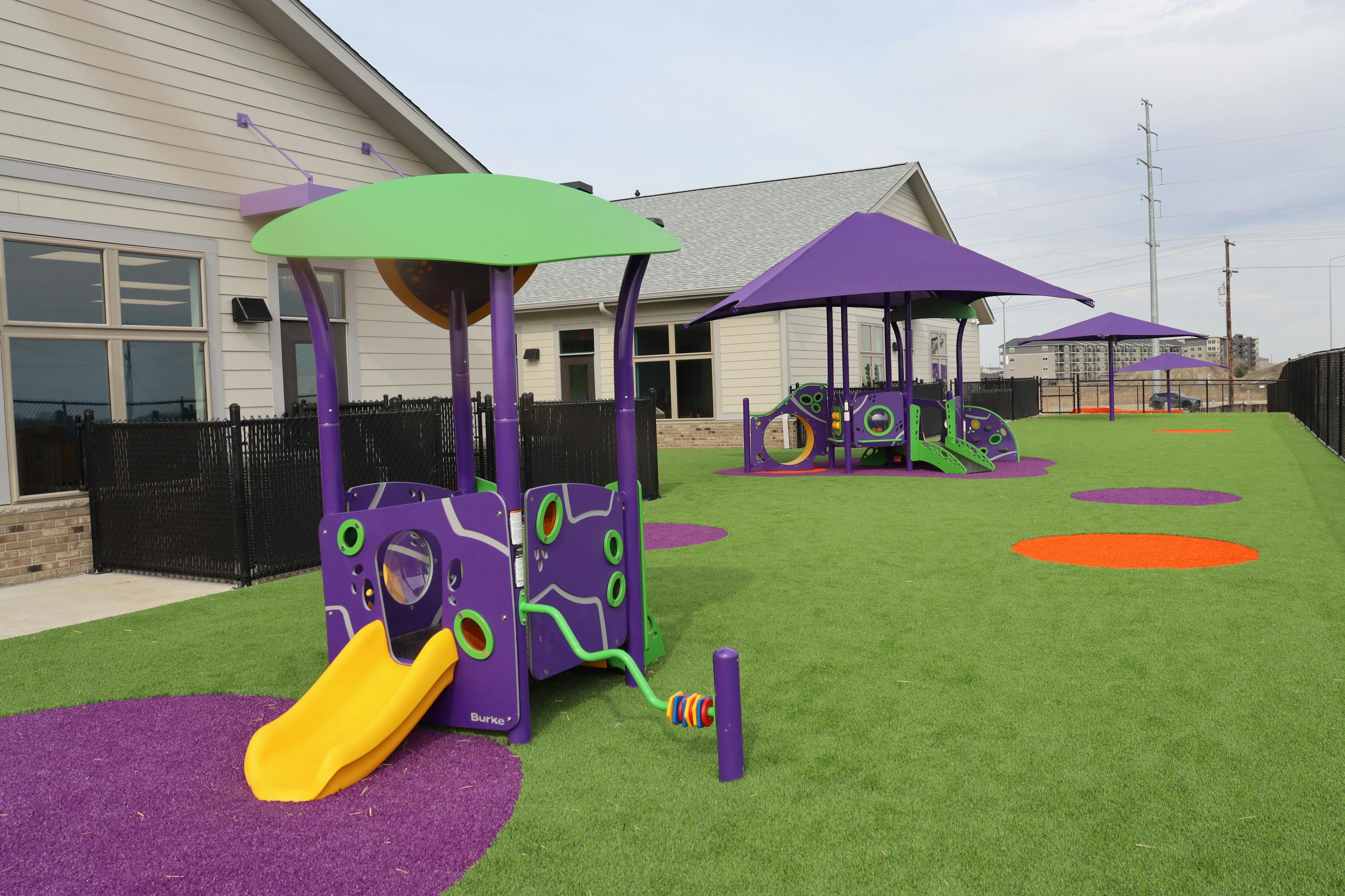 Playground area with purple and green play structures, yellow slide