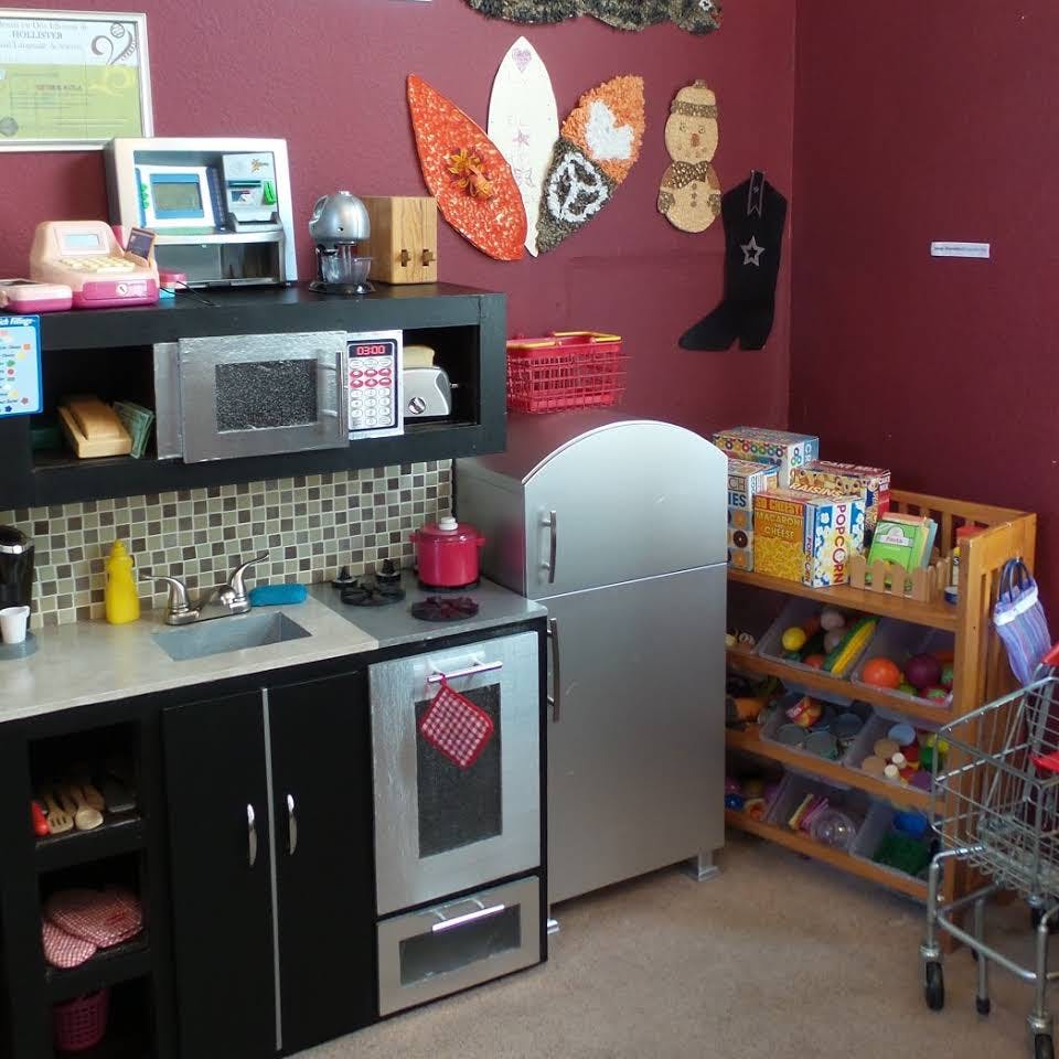 Play kitchen with microwave, sink, stove, refrigerator, and shelving unit