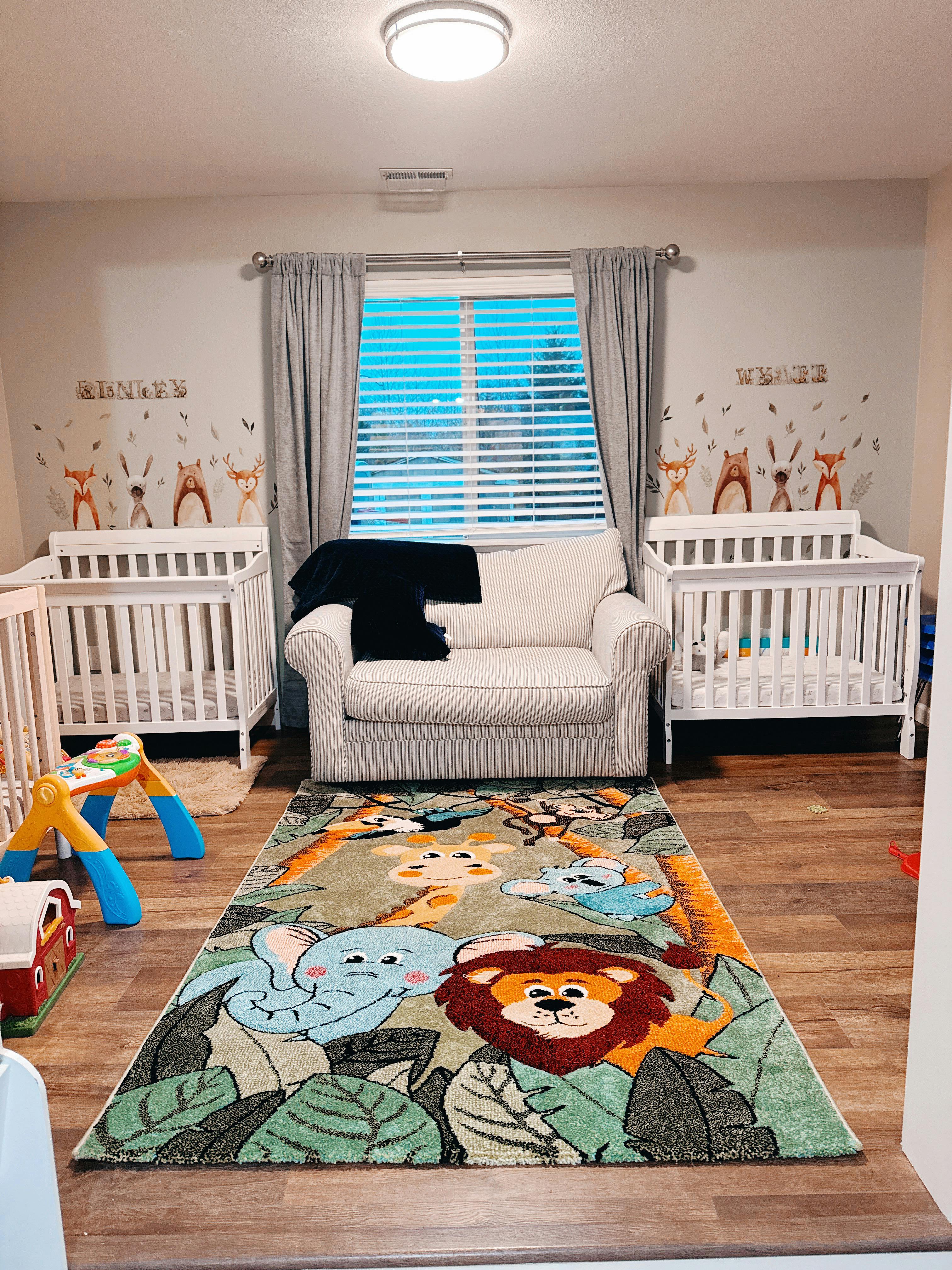 Nursery room with two white cribs, a white armchair, and a colorful rug