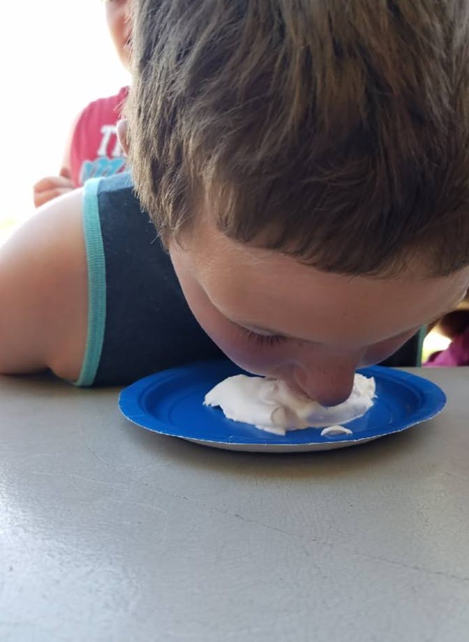 Child eating whipped cream from a blue plate