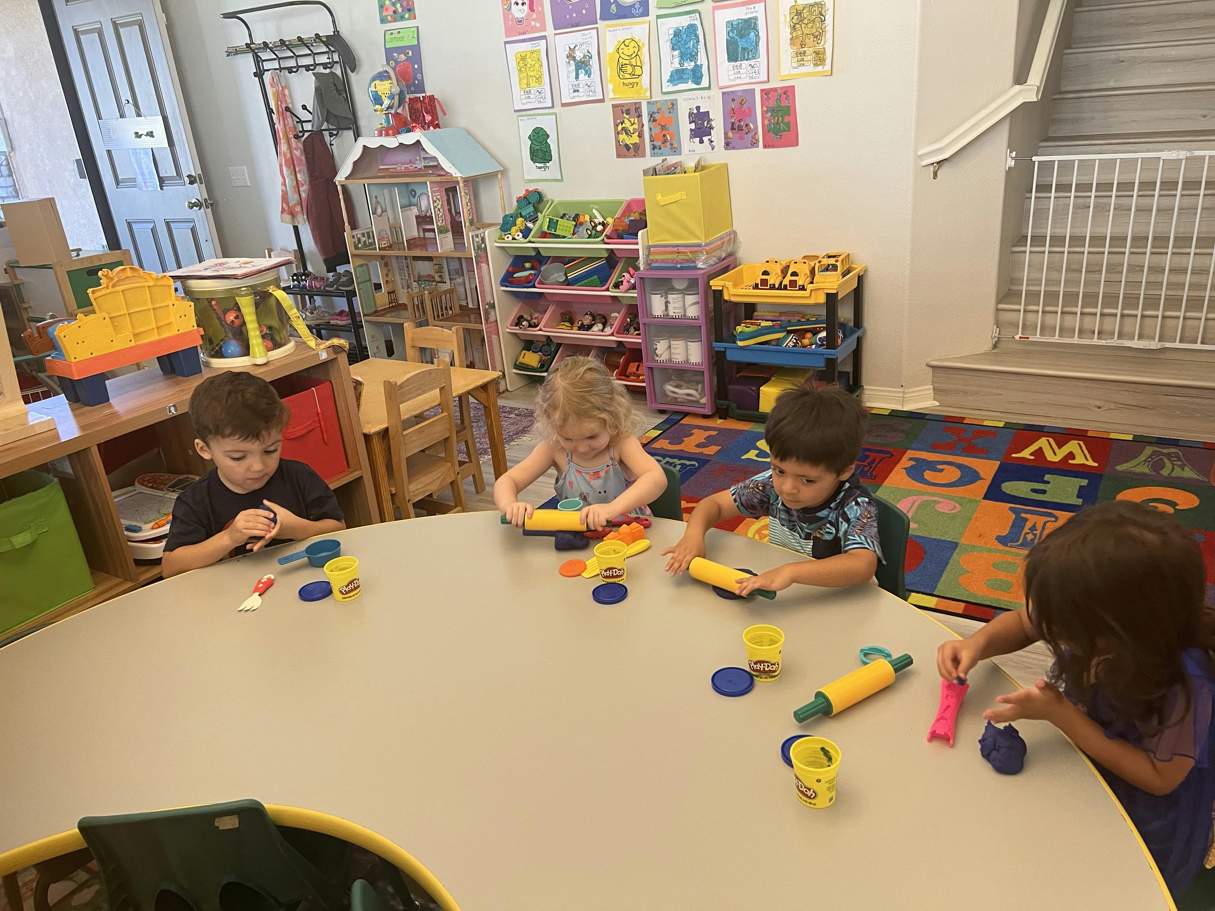 Four children playing with Play-Doh at a table in a classroom