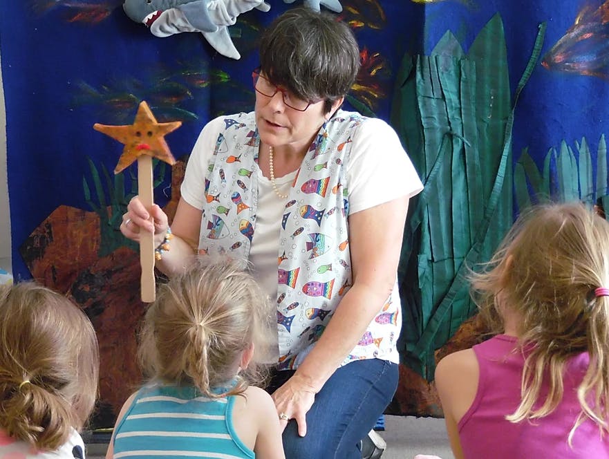 Person holding a star wand, speaking to three children