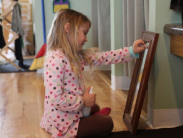 Child cleaning a mirror with a spray bottle