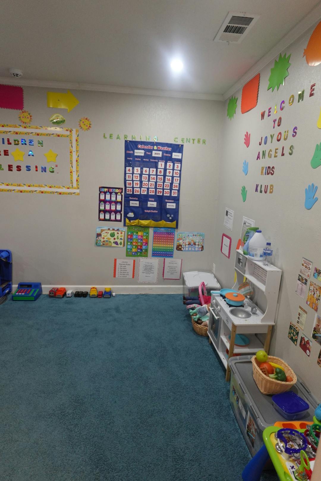 Children's play area with blue carpet, wall decorations, and toy kitchen