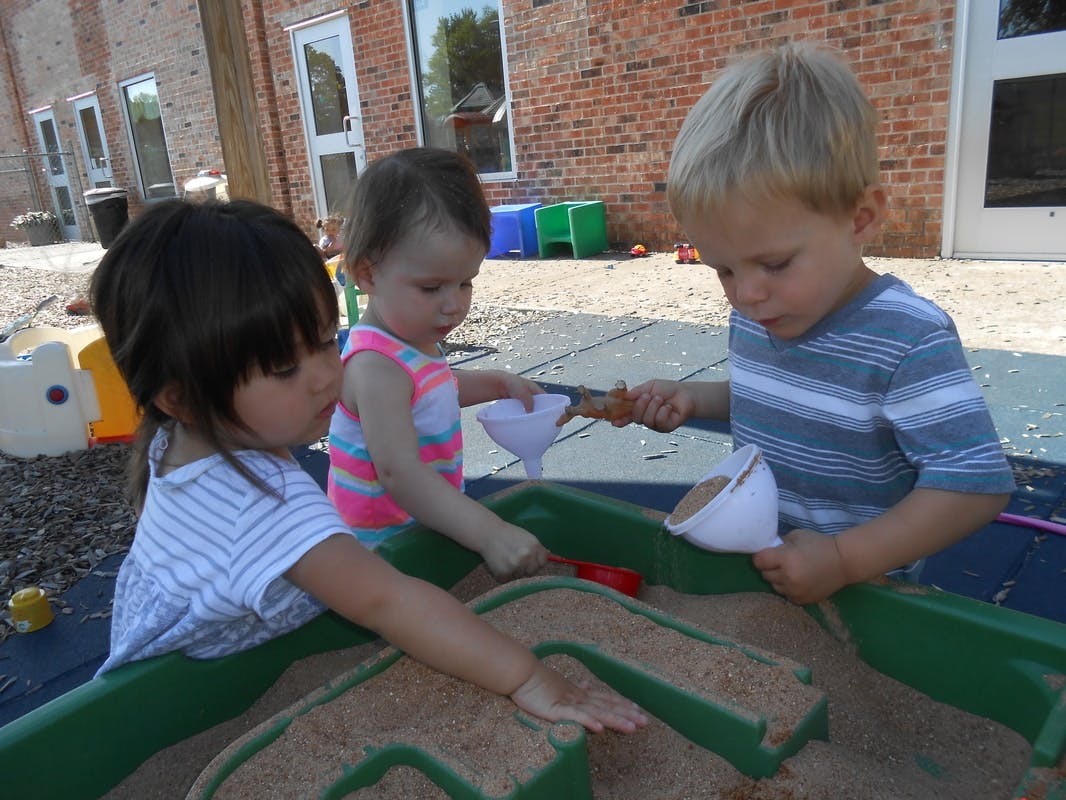Three children playing in a sandbox with sand and toys