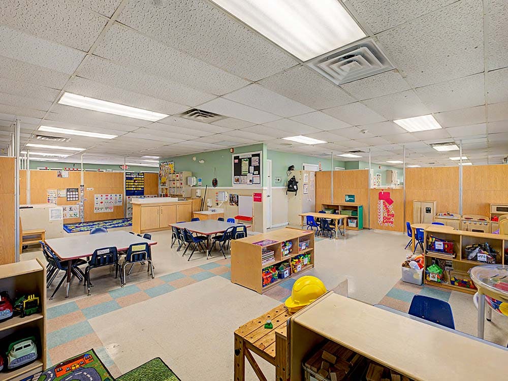 Empty classroom with small tables, chairs, and shelves full of toys
