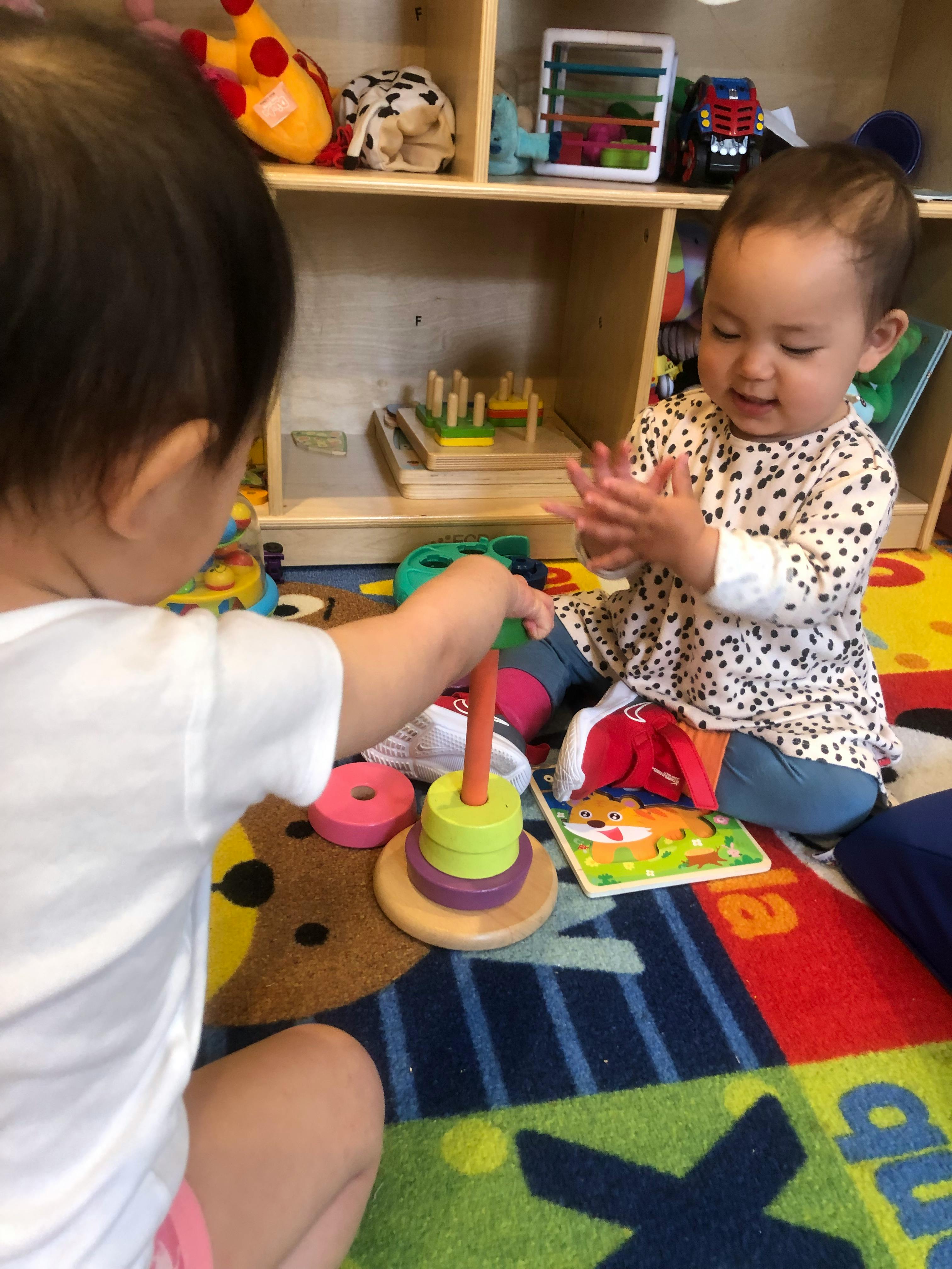 Two children playing with a stacking toy on a colorful rug