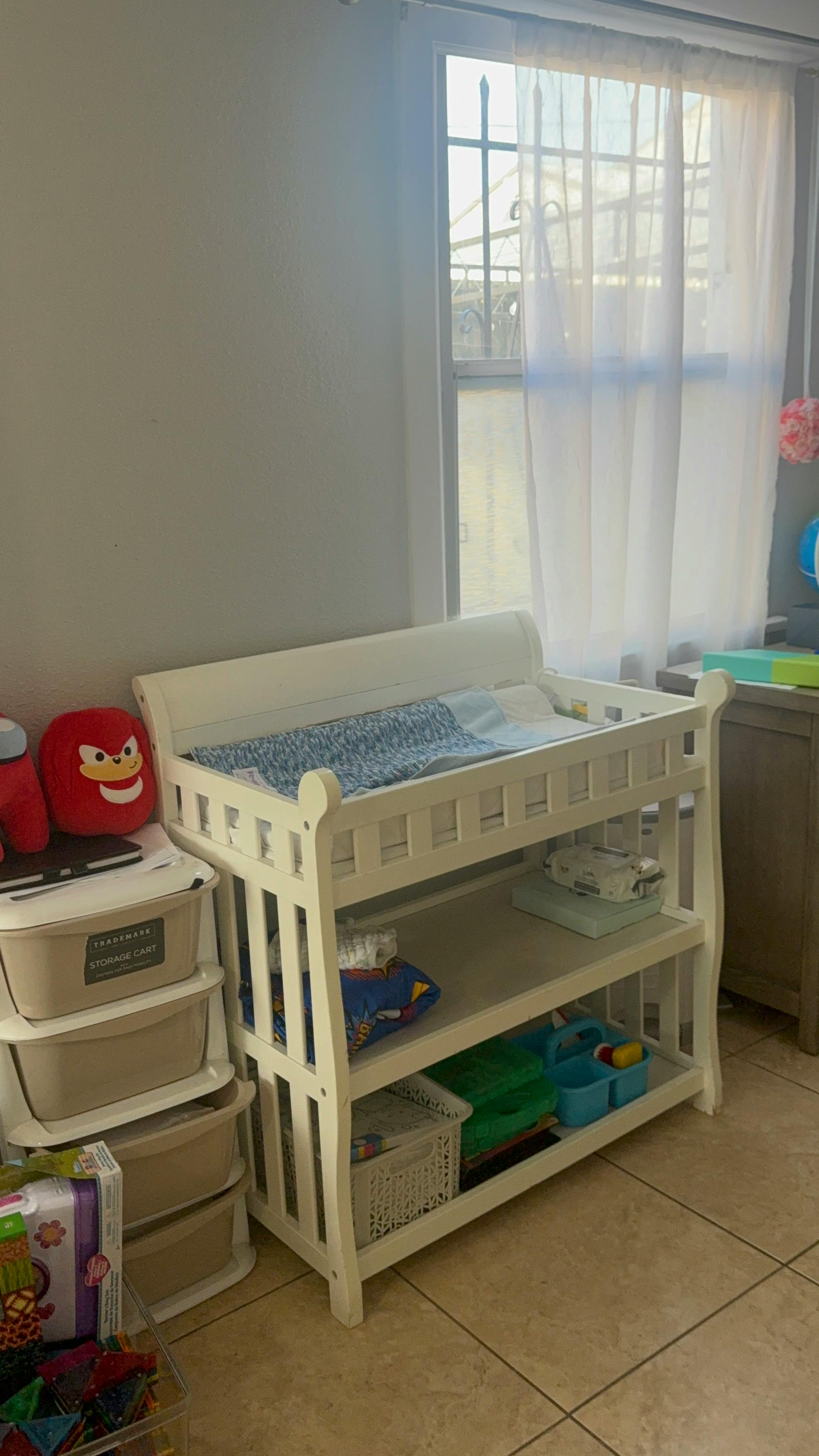 White changing table with baby supplies next to a window