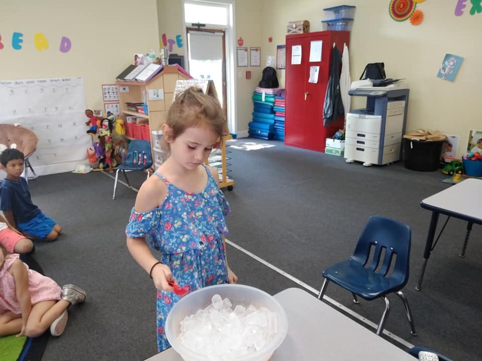 Child in a classroom holding a red scoop over a bowl of white objects