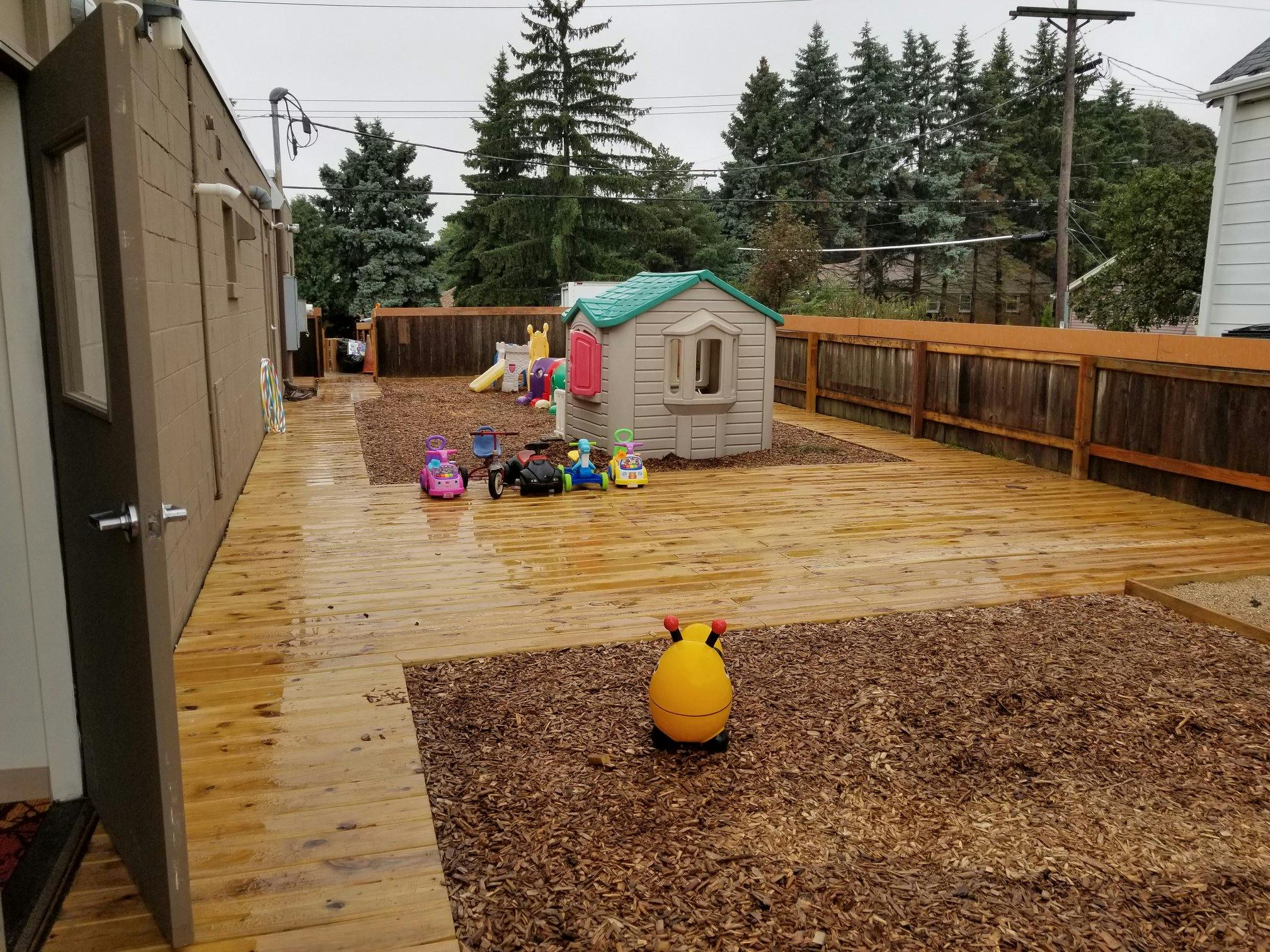 Outdoor play area with a wooden deck, playhouse, and wood chip ground