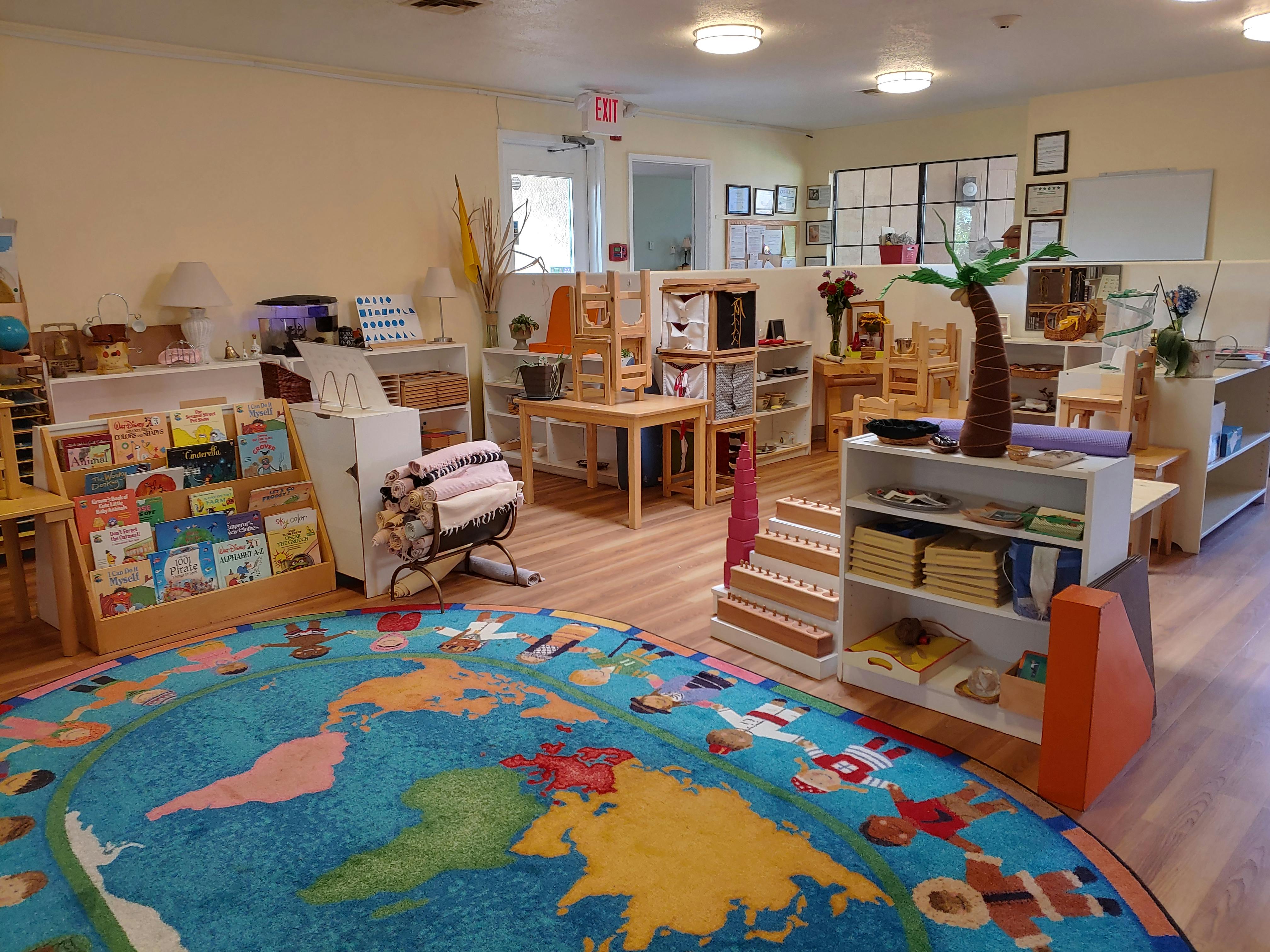Classroom with a world map rug, bookshelves, and small tables