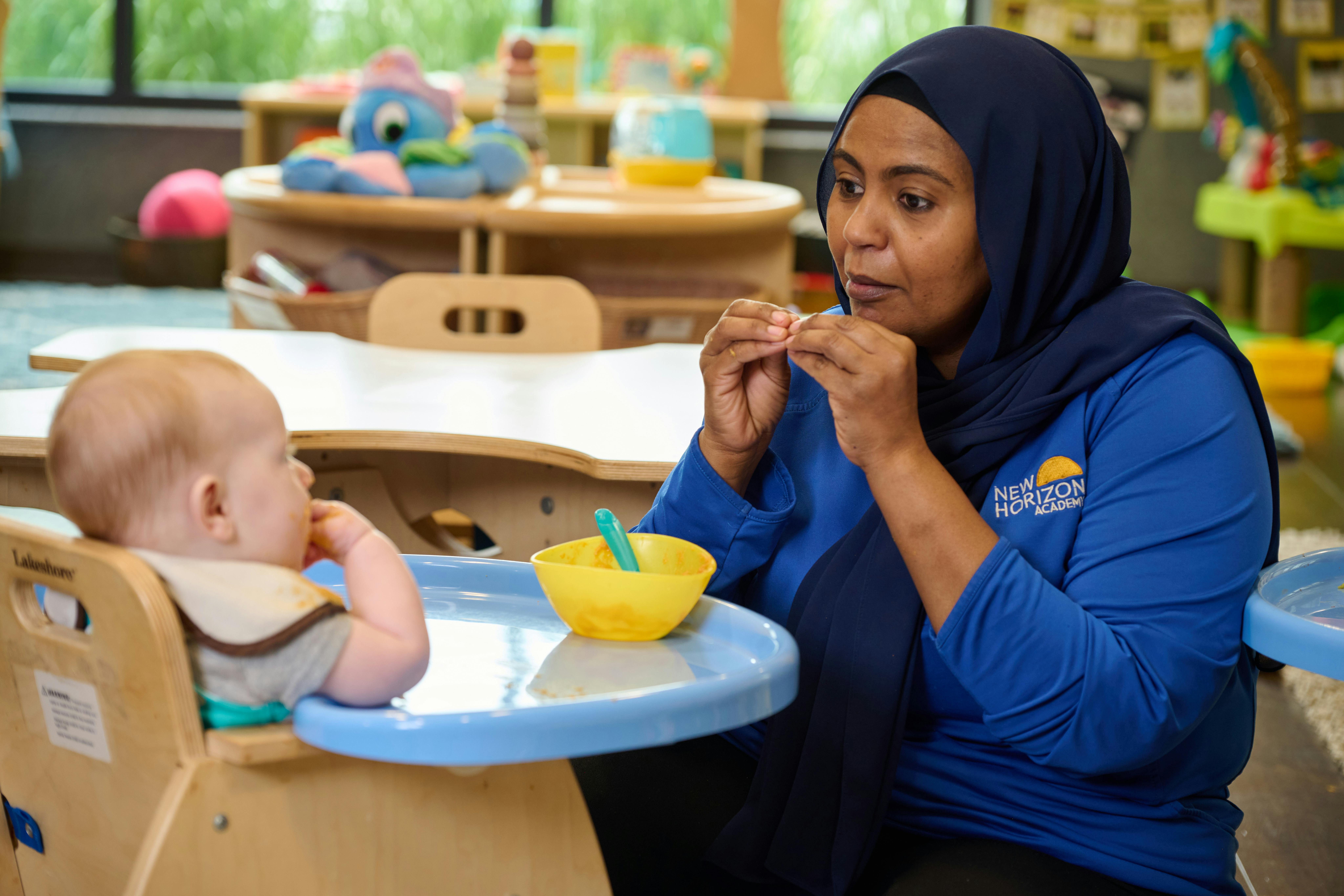 Person in hijab feeding a child in a high chair