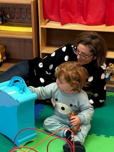 Person and child playing with toys on a green mat