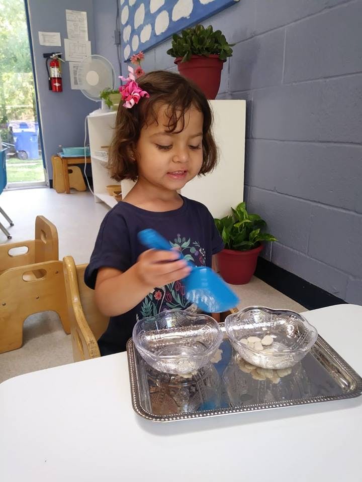 Child holding a blue scoop over two bowls on a tray