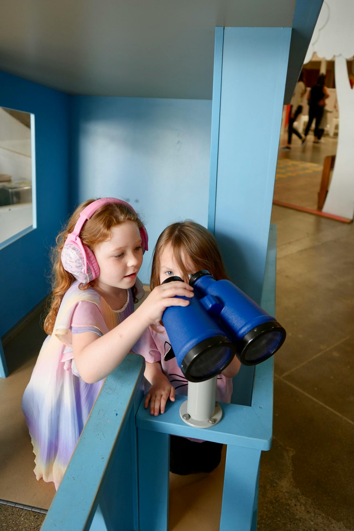 Two children playing with large blue binoculars in a blue play structure